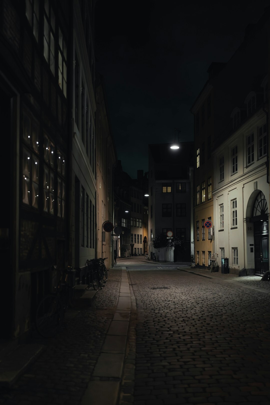 Empty foggy cobblestone street in an old town at night with warm street lamps