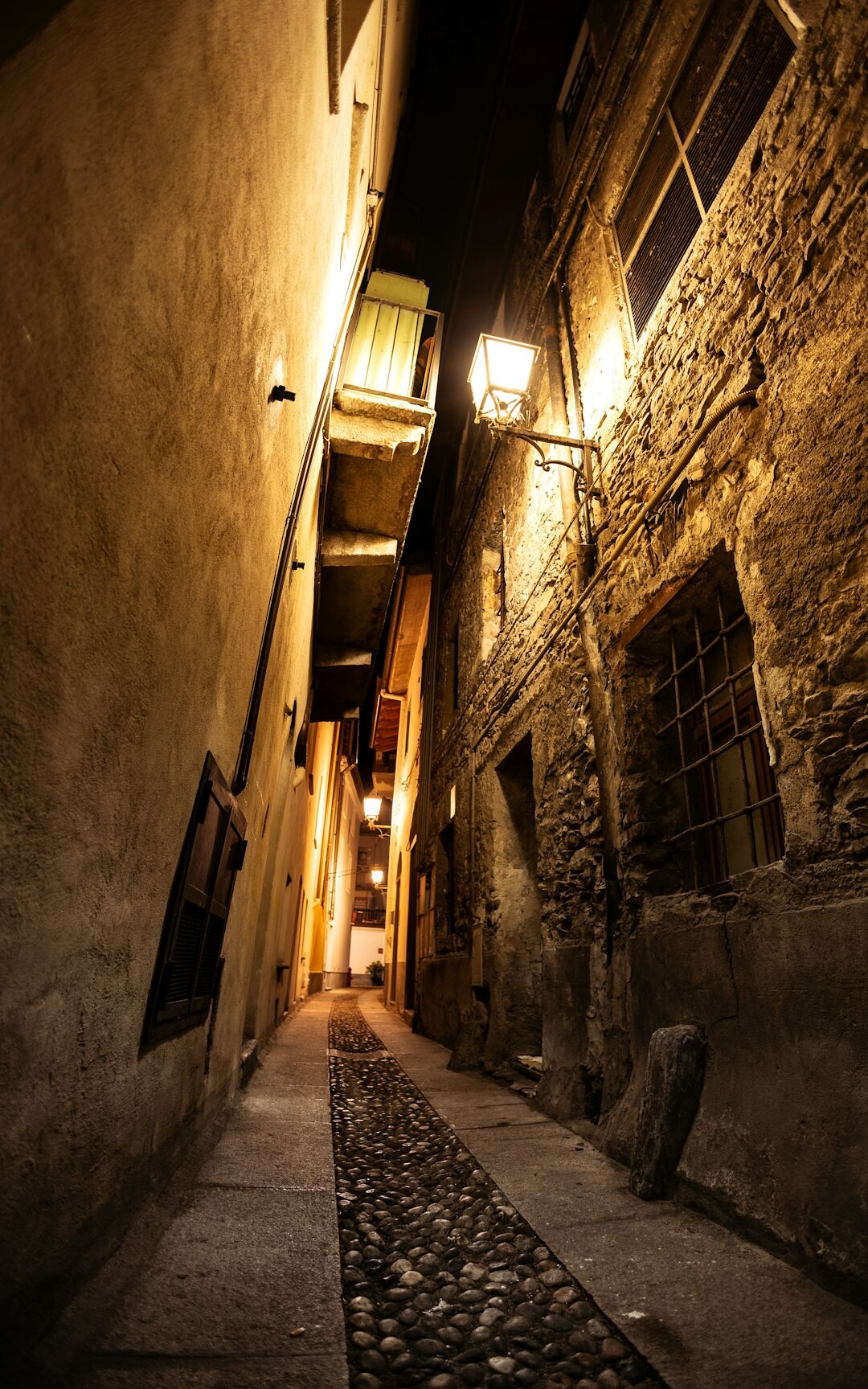 Narrow cobblestone alley in an old European town lit by a single lantern at night